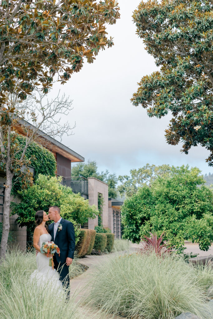Couple kisses among ornamental grasses outside the modern architecture of Bardessono during their Yountville elopement in Napa Valley